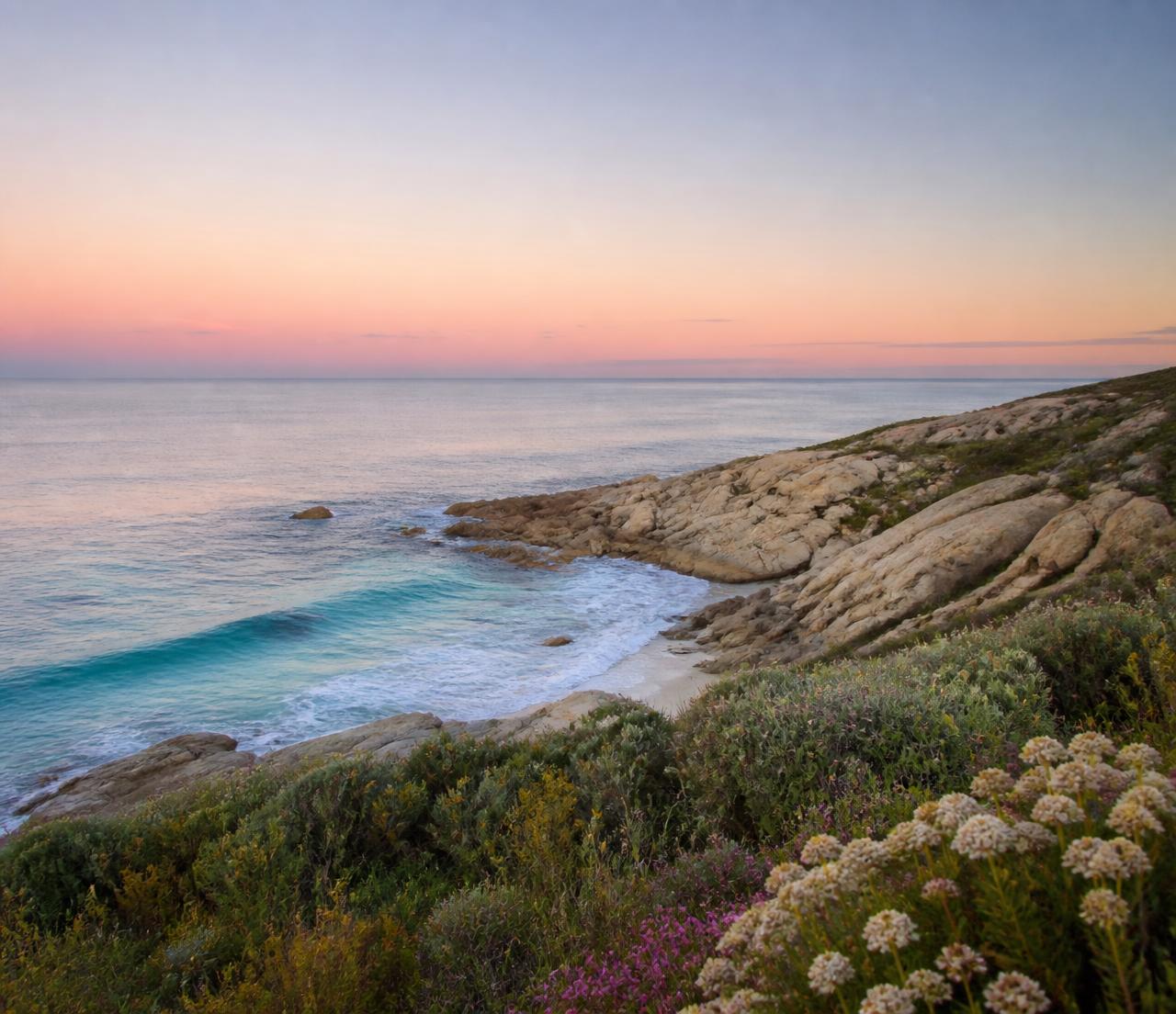 The Margaret River coastline at sunrise, with turquoise surf, granite rocks and coastal wildflowers